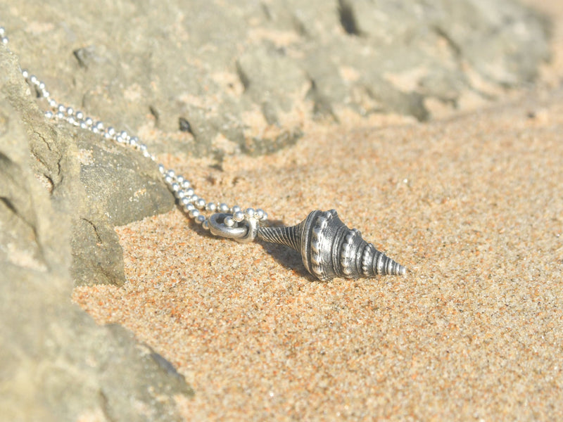 Con una elegancia sutil, el collar 'Susurro del Mar' presenta un colgante de concha con una forma espiral que evoca la delicadeza de las olas al tocar la orilla. Cada detalle finamente labrado en este adorno es un tributo a la riqueza visual del fondo marino. La textura palpable y el diseño intrincado de la espiral hacen que esta pieza sea un emblema de la sofisticación natural. Ideal para quien aprecia la belleza en su estado más puro y busca un toque de distinción en su estilo. Almakaia by Heike Otten.